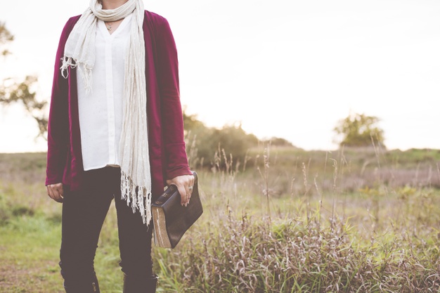closeup-shot-female-standing-grassy-field-while-holding-bible-with-blurred-background_181624-18164