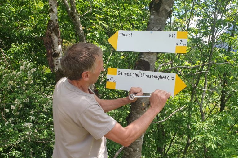 Un volontario del Gruppo Amici della Montagna di Cencenighe posiziona una tabella segnaletica