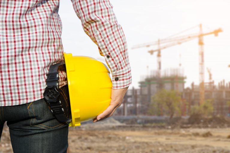 hand-s-engineer-worker-holding-yellow-safety-helmet-with-building-on-site-background