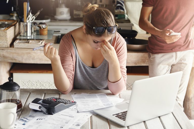 young-family-facing-debt-problems-stressed-woman-holding-her-head-in-frustration-doing-bank-accounts-and-making-necessary-calculations-using-laptop-and-calculator