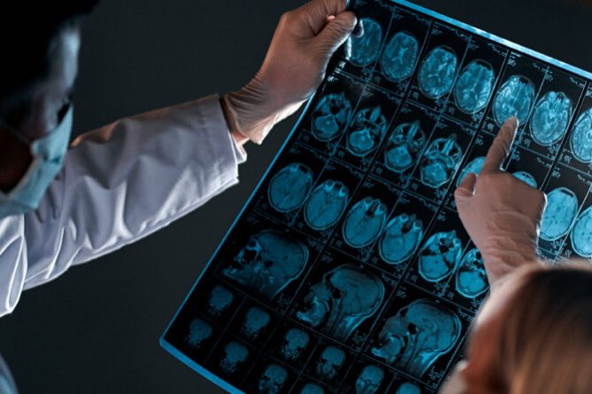 Two doctors in protective masks look and discuss an X-ray or MRI