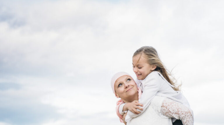 A woman with cancer is next to her daughter. A girl is hugging