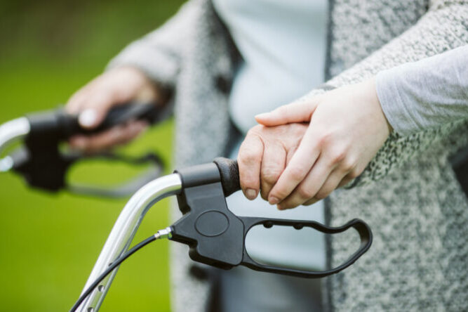 Senior woman with walker during walk in the park of modern nursing home